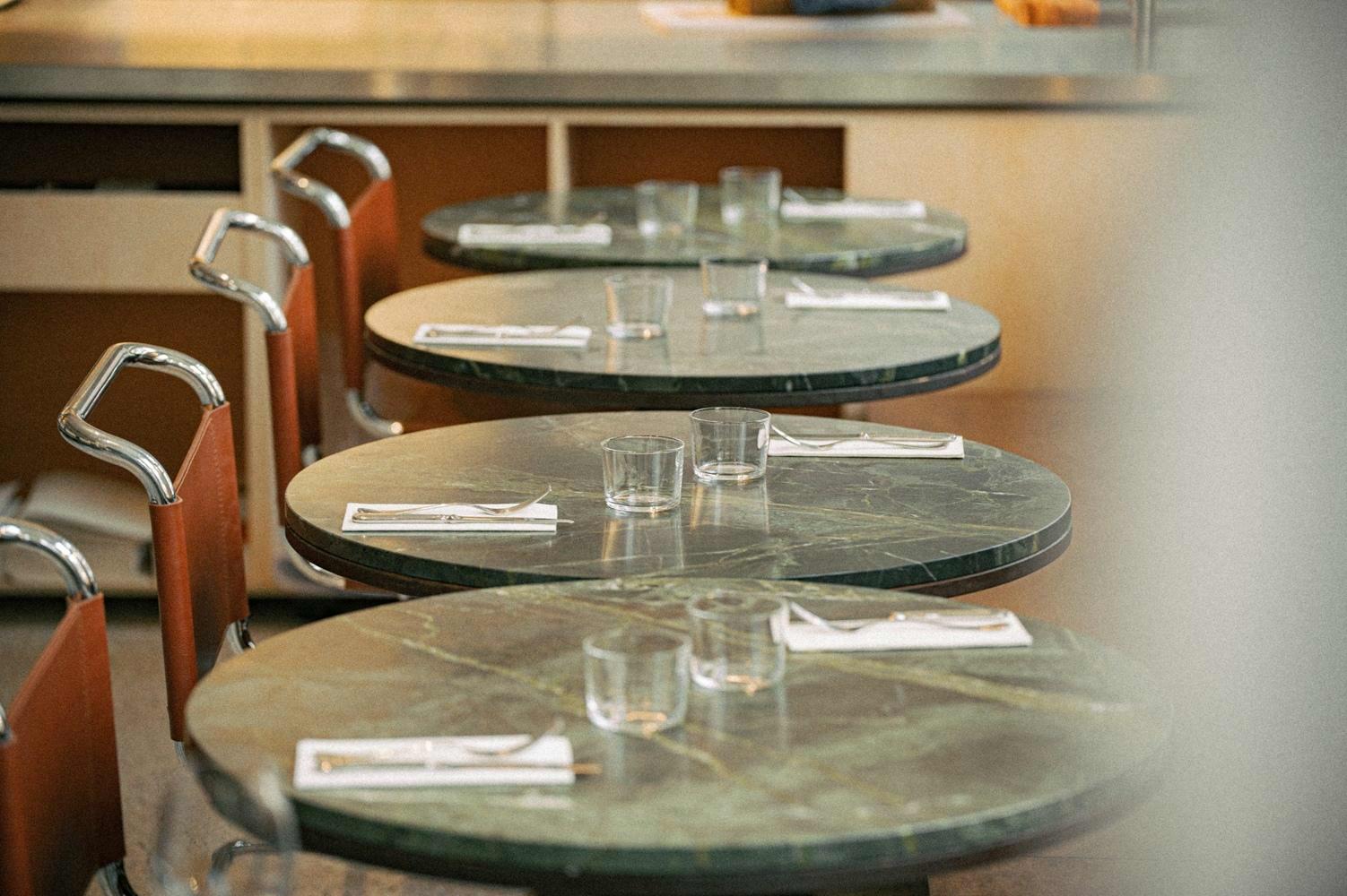 De granieten ronde tafeltjes in restaurant De Lieve zijn ingedekt met zilveren bestek en witte servetten.